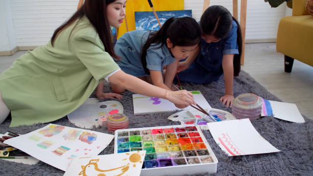 istock Asian two siblings learning study watercolor paint together at home. Teacher or parent teach student or daughter drawing paint color imagination on paper homework.Activity creativity education concept 1406676320