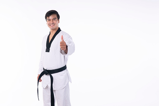 Confidence athlete strong young man wear uniform taekwondo with black belt showing thumbs up while standing over isolated white background. Activity power tradition concept.