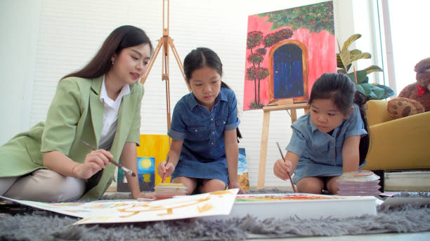 istock Asian two siblings learning study watercolor paint together at home. Teacher or parent teach student or daughter drawing paint color imagination on paper homework.Activity creativity education concept 1406676357