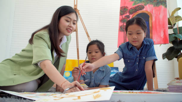 istock Asian two siblings learning study watercolor paint together at home. Teacher or parent teach student or daughter drawing paint color imagination on paper homework.Activity creativity education concept 1406676365