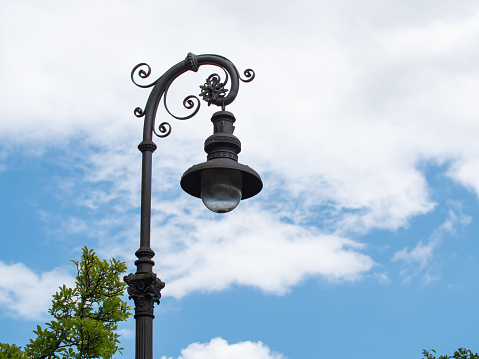 Historic street lamp in the park. Blue sky and clouds in the background.