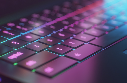 A conceptual gaming laptop for the e-sport gamer on the move. A computer generated 3D render in neon light and moody mist. Camera framing the WASD buttons.