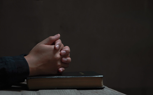 Close-up women christian read bible. Hands folded in prayer on a Holy Bible on wooden table.