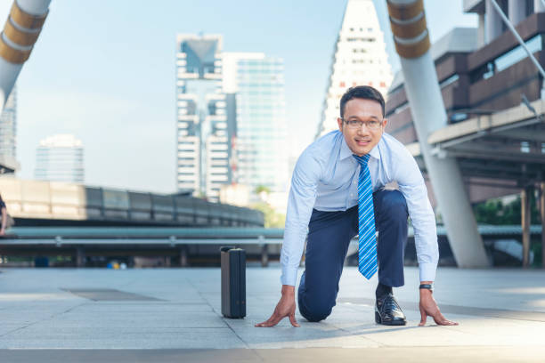 Businessman start kneeling city street race business goal winner challenge. Asian man look at camera smile face wear glasses. Man happiness time start up a business goal. Businessman race concept stock photo