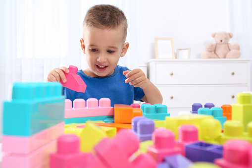Cute little boy playing with colorful building blocks at table in room