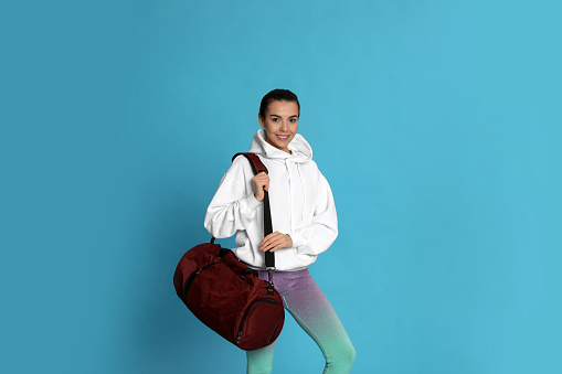Beautiful woman with sports bag on light blue background