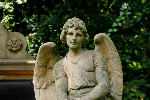 head shot of an angel with wings wide-spread looking down at the grave below