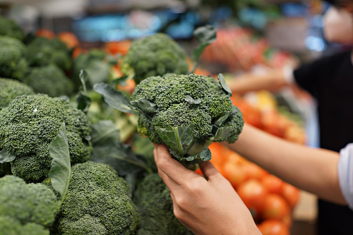 Woman's hand choosing fresh broccoli in supermarket. Concept of healthy vegetarian food.