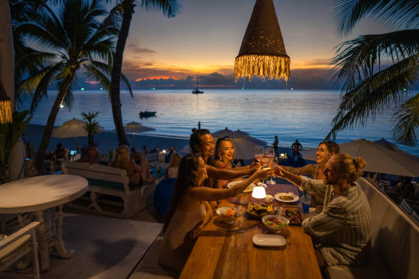 Multiracial friends at the dinner at the beach restaurant toasting with wine Group of multiracial friends enjoy the dinner party with food and drinks at the beach restaurant during sunset beach bar stock pictures, royalty-free photos & images