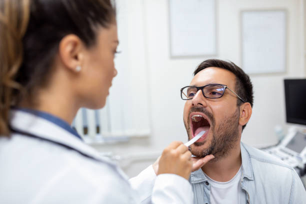 male patient opening his mouth for the doctor to look at his throat. female doctor examining sore throat of patient in clinic. otolaryngologist examines sore throat of patient. - doctor patient male tongue depressor imagens e fotografias de stock