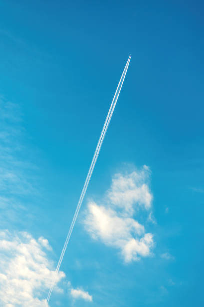 Airplane vapor trail or contrail pattern on blue sky with clouds from below