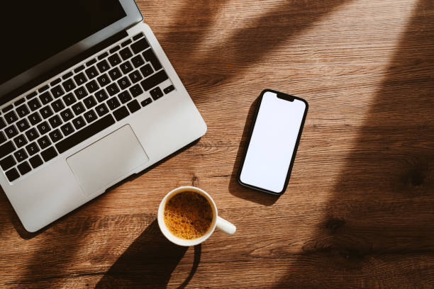 istock Cup of coffee, laptop computer and smartphone with blank white mockup screen on office work desk 1406685232