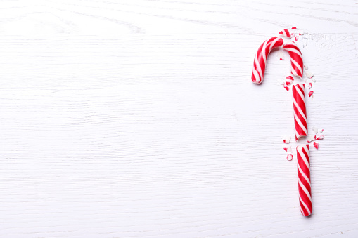 Broken sweet Christmas candy cane on white wooden table, top view. Space for text