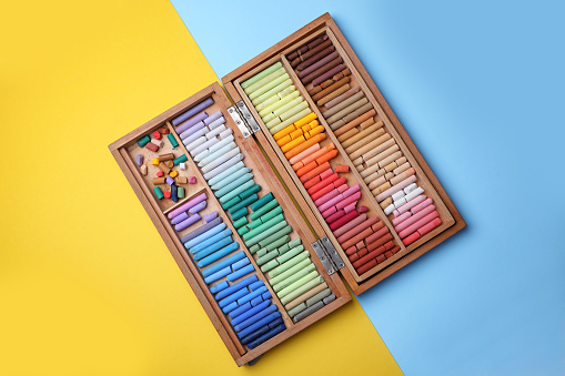 Drawing pastel set in wooden box on color background, top view