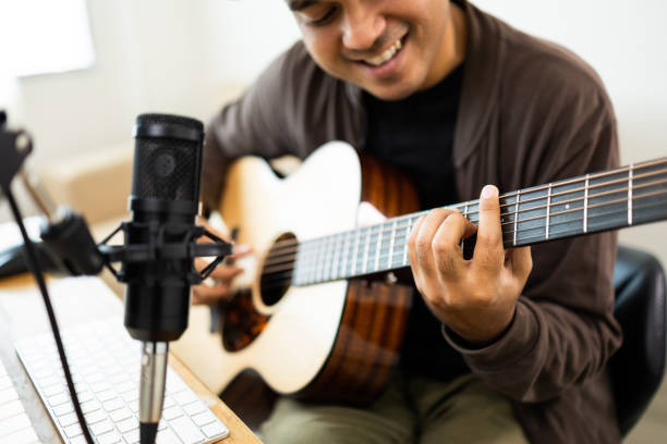 istock Professional Musician with condenser microphone and tablet for Mixing Mastering music. Hispanic male composing a song with guitar and piano keyboard at digital Recording home studio 1406687714