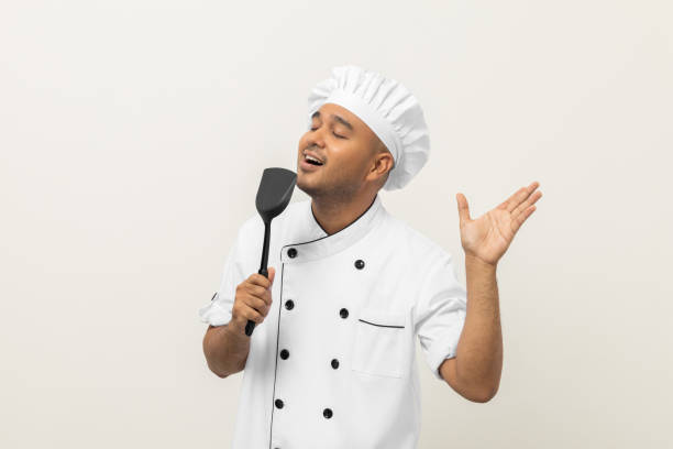istock Super star singing masterchef. Young happy asian chef wearing uniform enjoy with singing voice and dancing in the kitchen on isolated white background. Indian man Occupation restaurant and hotel. 1406688519