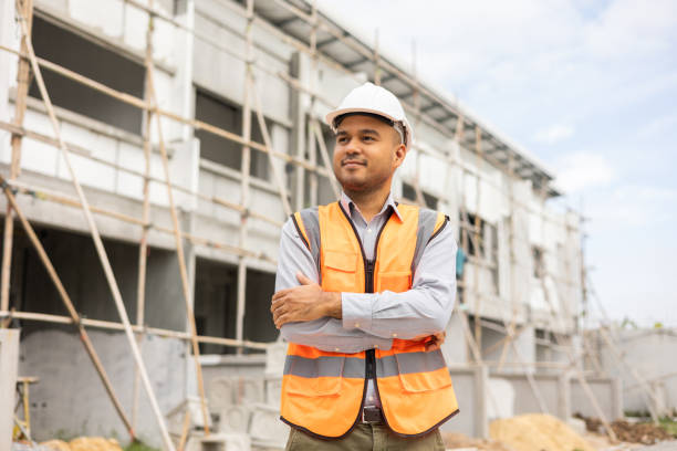 istock Confident engineer handsome man standing arms crossed at modern home building construction. Architect with white safety helmet at construction site. 1406689002