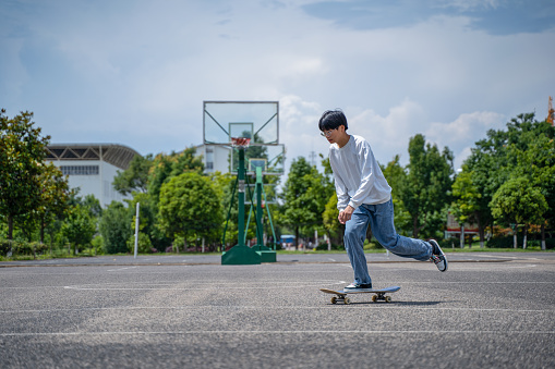 an asian chinese teenage boy practicing skateboarding and learning new skill at public park weekend morning