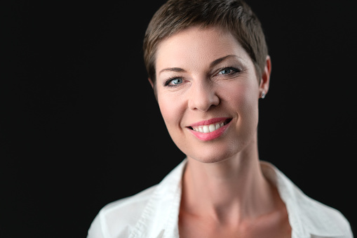 Soft studio portrait of attractive short haired smiling business woman in white shirt on black background. Concept for positive thinking, business success, work attitude, satisfaction, reliability