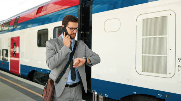 homme d’affaires adulte vérifiant l’heure sur sa montre-bracelet à la gare tout en parlant au téléphone - vérifier lheure photos et images de collection