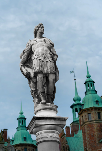 Hillerød, Denmark - June 30th 2022: Statue in stone placed on a pillar. Depiction of a centurion or Greek god. Shallow depth of field with blurred background.