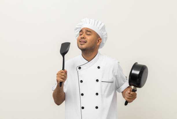 istock Super star singing masterchef. Young happy asian chef wearing uniform enjoy with singing voice and dancing in the kitchen on isolated white background. Indian man Occupation restaurant and hotel. 1406691738