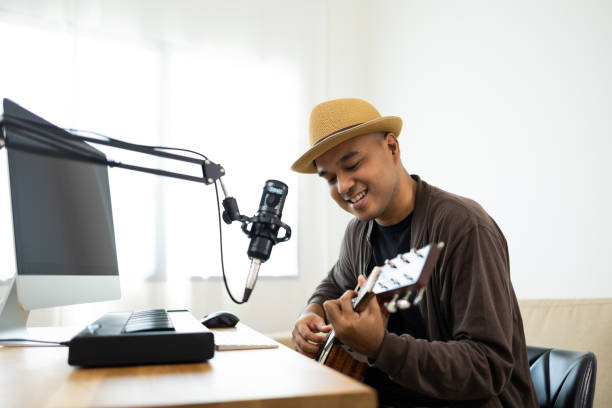 istock Professional Musician with condenser microphone and tablet for Mixing Mastering music. Hispanic male composing a song with guitar and piano keyboard at digital Recording home studio 1406691778