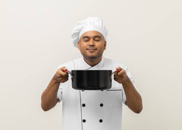 istock Smiling Young man chef in uniform gesture smelling empty hot pot stew soup delicious dish menu good taste on isolated. Cooking man Occupation chef People in kitchen restaurant and hotel. 1406692068