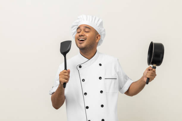 istock Super star singing masterchef. Young happy asian chef wearing uniform enjoy with singing voice and dancing in the kitchen on isolated white background. Indian man Occupation restaurant and hotel. 1406692082