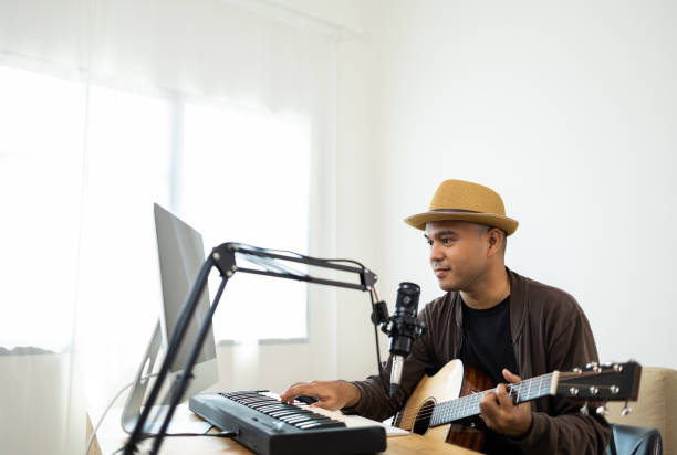 istock Professional Musician with condenser microphone and tablet for Mixing Mastering music. Hispanic male composing a song with guitar and piano keyboard at digital Recording home studio 1406692109