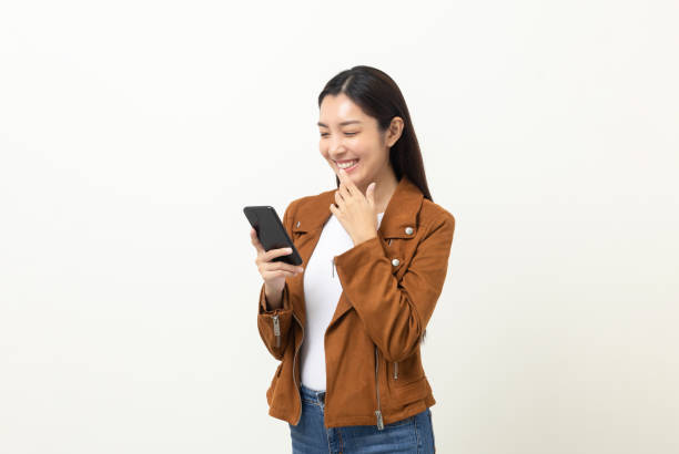 istock Pretty young asian woman using smartphone standing on isolated white background. She texting on cell phone. Dressing with jacket and jean. 1406692117