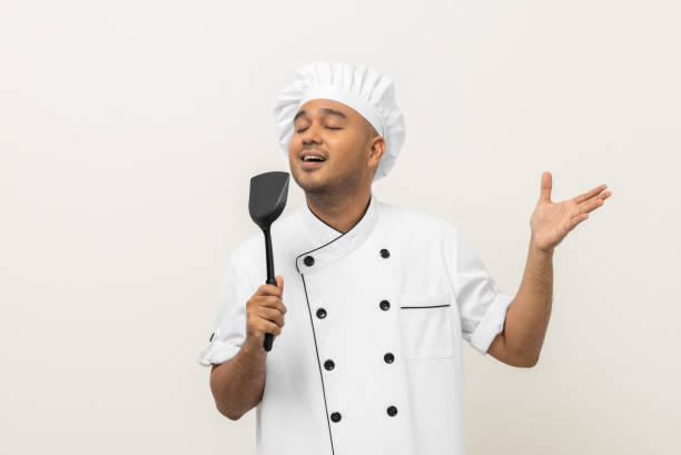 istock Super star singing masterchef. Young happy asian chef wearing uniform enjoy with singing voice and dancing in the kitchen on isolated white background. Indian man Occupation restaurant and hotel. 1406692479