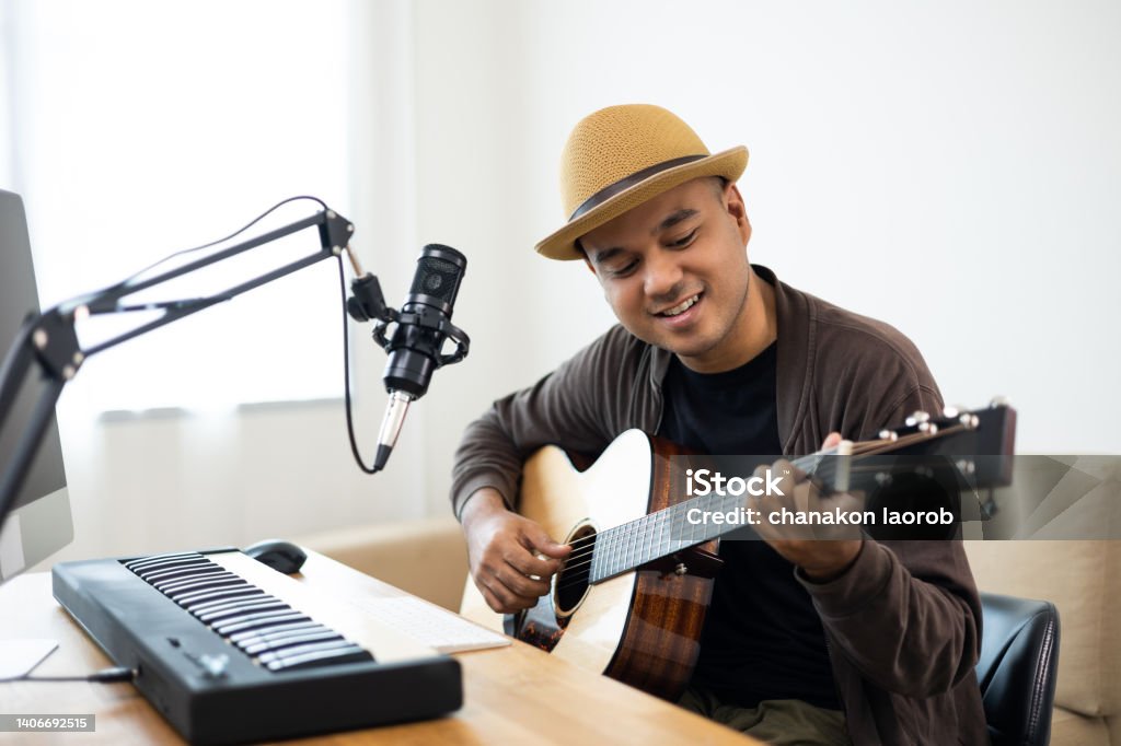 Professional Musician with condenser microphone and tablet for Mixing Mastering music. Hispanic male composing a song with guitar and piano keyboard at digital Recording home studio Music Stock Photo