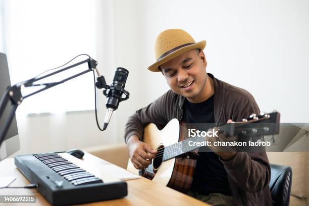 Professional Musician With Condenser Microphone And Tablet For Mixing Mastering Music Hispanic Male Composing A Song With Guitar And Piano Keyboard At Digital Recording Home Studio Stock Photo - Download Image Now