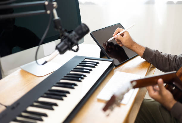 istock Close up hands song writer composing music note on tablet. Professional composer Recording Mixing and Mastering in home studio with keyboard and guitar. Digital music production 1406692535