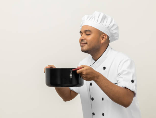 istock Smiling Young man chef in uniform gesture smelling empty hot pot stew soup delicious dish menu good taste on isolated. Cooking man Occupation chef People in kitchen restaurant and hotel. 1406693093
