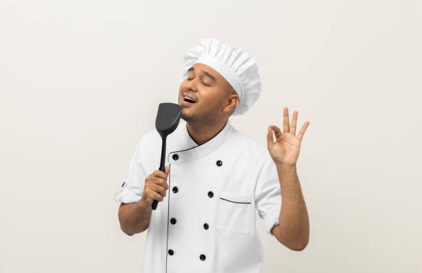 istock Super star singing masterchef. Young happy asian chef wearing uniform enjoy with singing voice and dancing in the kitchen on isolated white background. Indian man Occupation restaurant and hotel. 1406693122