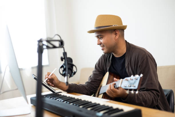 istock Professional Musician song writer with condenser microphone note on tablet. Hispanic male composing a song with guitar and piano keyboard at digital Recording home studio for Mixing Mastering music 1406693154