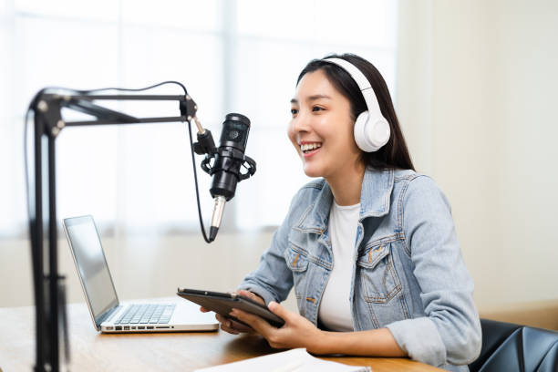 istock Content creator woman host streaming her a podcast on laptop with headphones and microphone interview cheering guest conversation at broadcast studio. Blogger motivation recording voice over radio. 1406693921