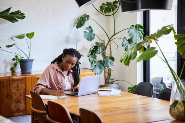 istock Young woman writing notes while working remotely from home on a laptop 1406697609