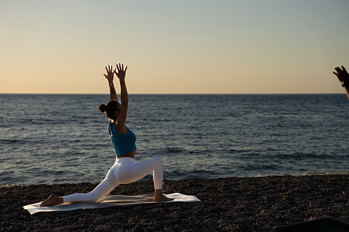 beautiful woman practicing yoga by the sea at sunrise