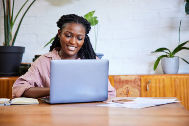 istock Smiling young woman working online from home using a laptop 1406697980
