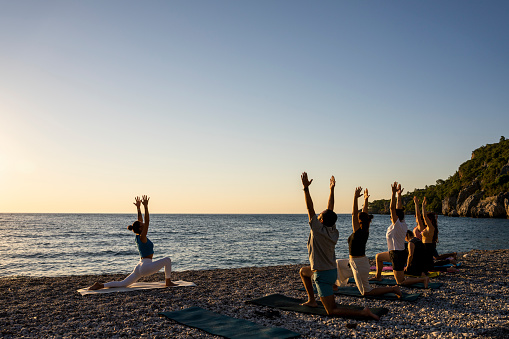 group of people practicing yoga on the beach at sunrise