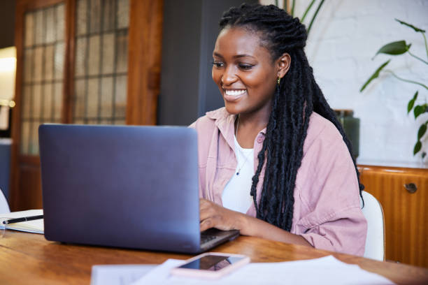 istock Smiling young woman working remotely on a laptop at a table at home 1406698087