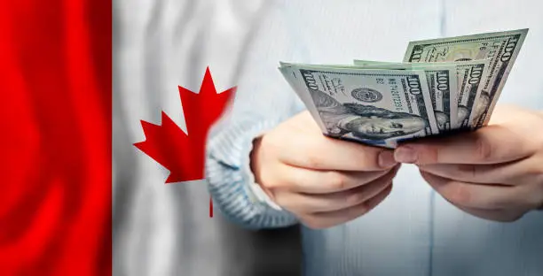 Photo of Currency exchange, finanse, banking and saving money in Canada. US dollars cash on Canadian flag background