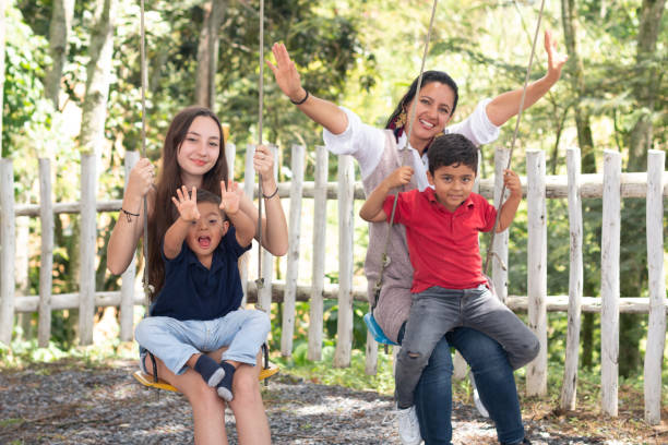 behinderter junge, der spaß im park hat, während seine familie auf einer schaukel fährt und in die kamera schaut. - sibling brother family with three children sister stock-fotos und bilder