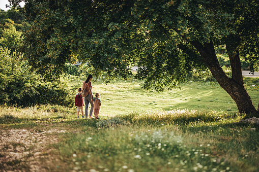 Family of three, mother with her little son and daughter taking a walk together on a meadow in nature.