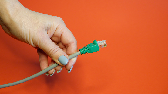 Green RJ45 network connector on a red background in well-groomed female hands