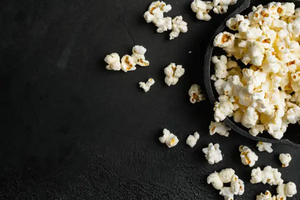 Tasty salted popcorn, on black dark stone table background, top view flat lay, with copy space for text