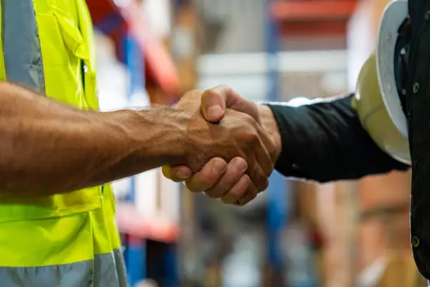 Caucasian man engineer shaking hands with factory manager in manufacturing warehouse. Male warehouse worker working and discussion with supervisors. Business industry engineering and manufacturing technology concept.